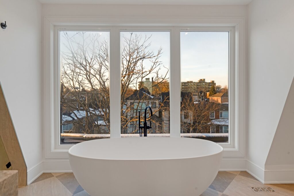 White freestanding bathtub beneath a large window, with a floor grille beside it.
