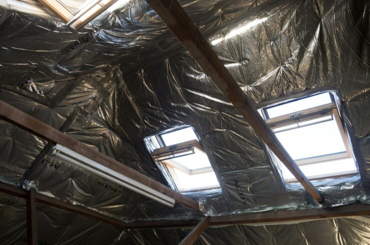 Reflective insulation lines an unfinished attic roof around timber beams and skylights.