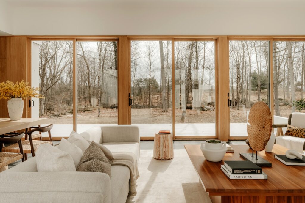 Daylight fills a living room through tall wood-framed windows and sliding glass doors.