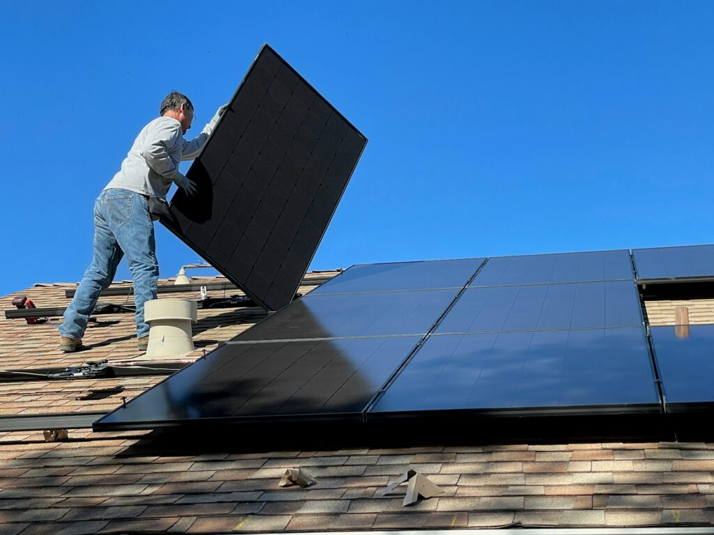 Worker installing a solar panel on a shingled roof
