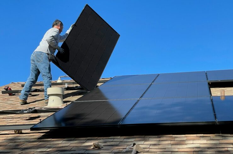 Worker installing a solar panel on a shingled roof